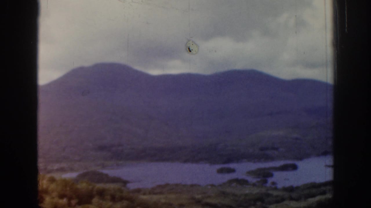 1961 Ireland 8mm frame showing a blue river or lake below purple-brown hills beneath heavy cloud, with visible film gate edges.