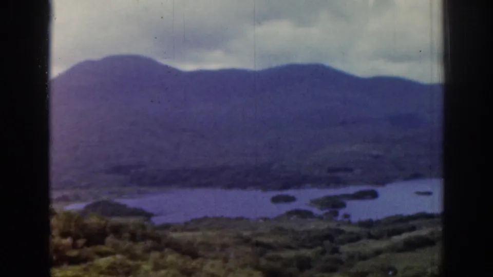 1961 Ireland travel frame with blue water, small islands or peninsulas, and purple hills under a cloudy sky.