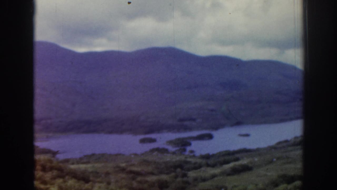 1961 Ireland 8mm view across blue water toward dark hills, with green-brown shoreline and soft motion blur.
