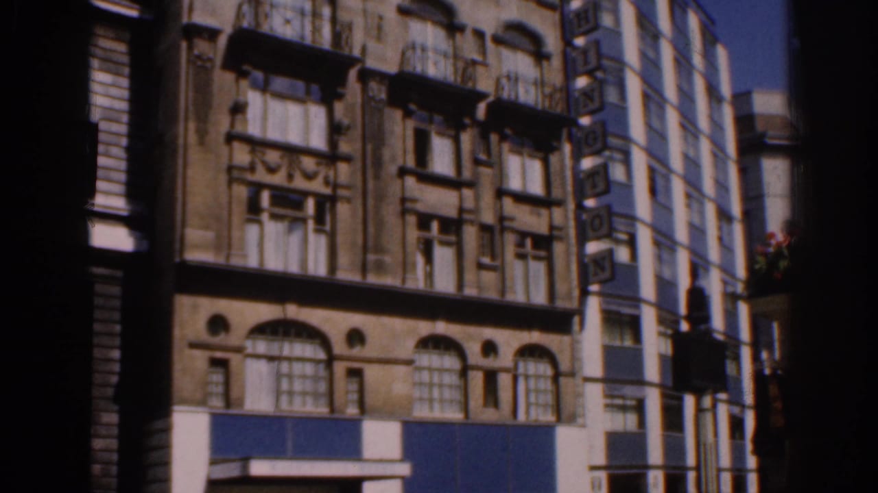 1961 Ireland home-movie frame showing lower facade details, arched windows, blue panels, and a side WASHINGTON sign.