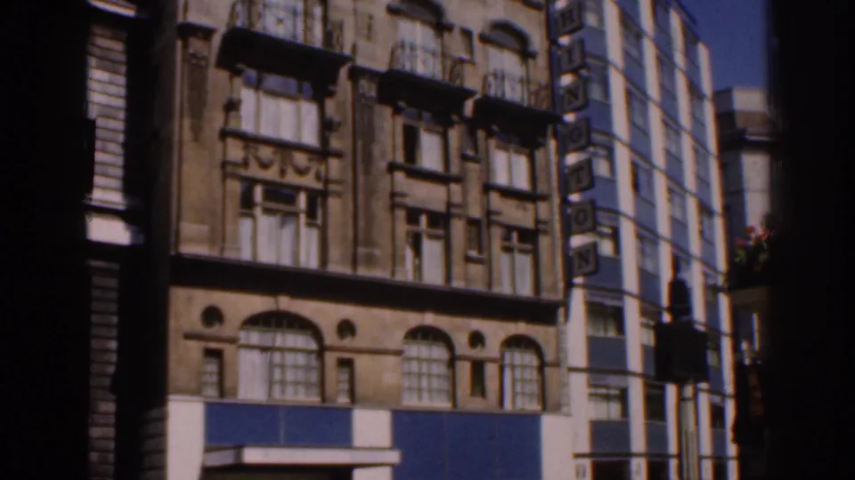 1961 Ireland home-movie frame showing lower facade details, arched windows, blue panels, and a side WASHINGTON sign.