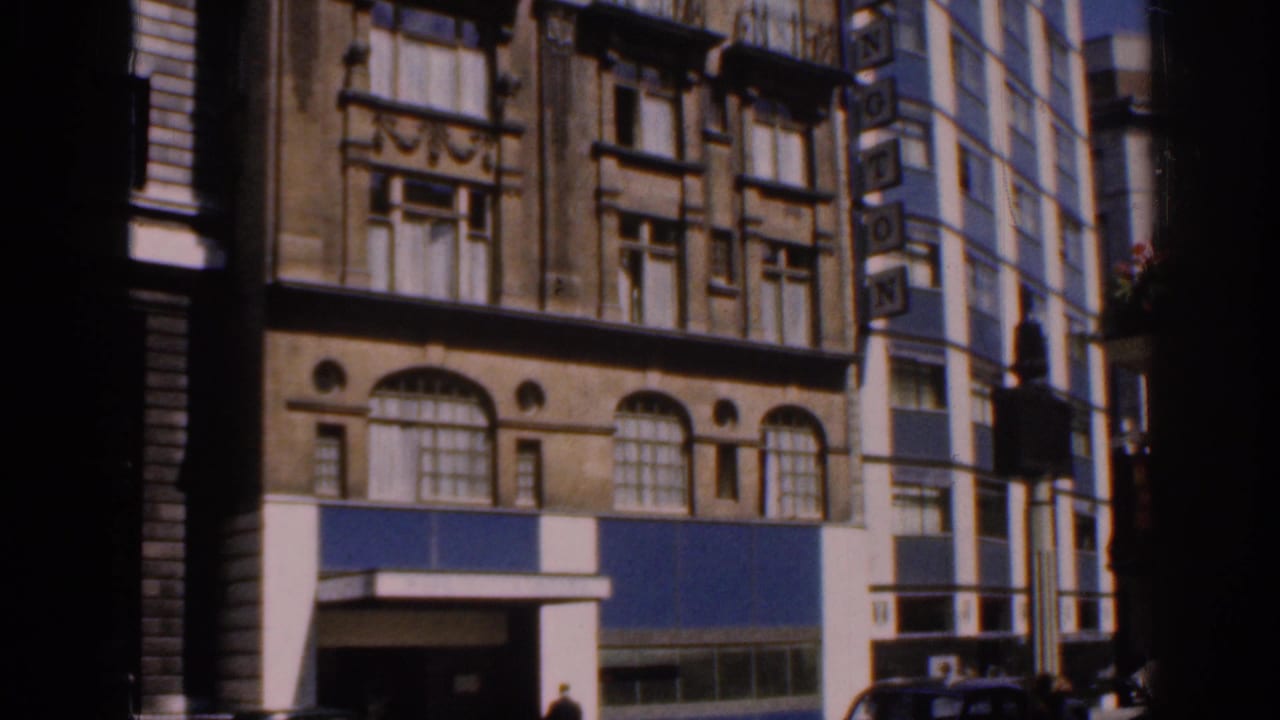 Similar street view of the arched-window building beside a taller modern facade.