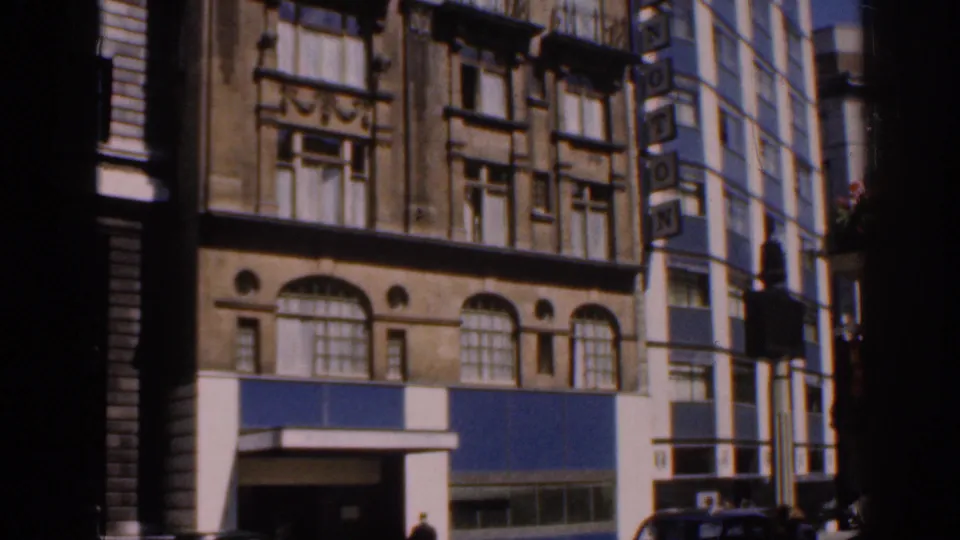 London street scene with an older arched-window facade, blue storefront panels, and a taller neighboring building partly in view.