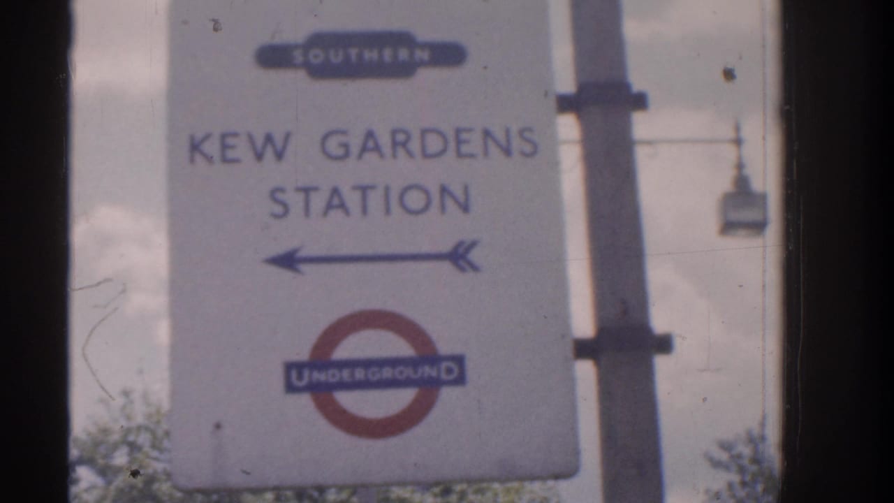 Kew Gardens Station sign showing an Underground roundel, overground wording, and a left-pointing arrow on a pale signboard.