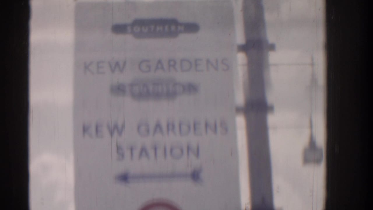 Blurred Kew Gardens Station sign seen through dark film-frame edges.