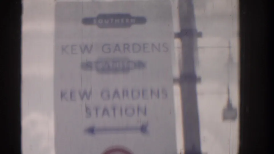 Blurred 8mm view of the Kew Gardens Station direction sign, with transit markings partly obscured by motion and frame edges.