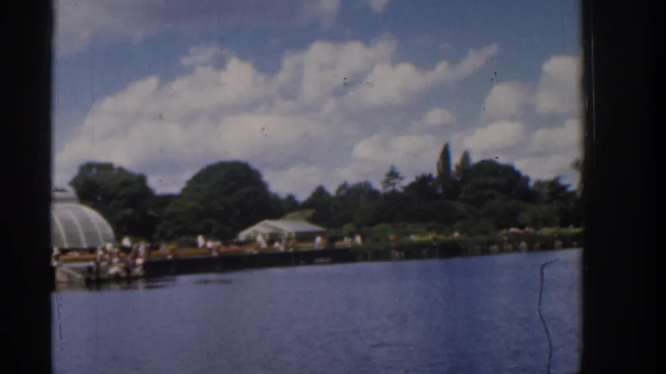 1961 Ireland lakeside view with a glasshouse-like structure, white shelter, water, trees, and distant people along the promenade.