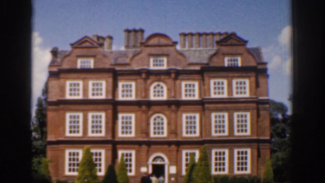 1961 Ireland 8mm frame showing a stately red brick mansion facade with white-trimmed windows, chimneys, and manicured shrubs.