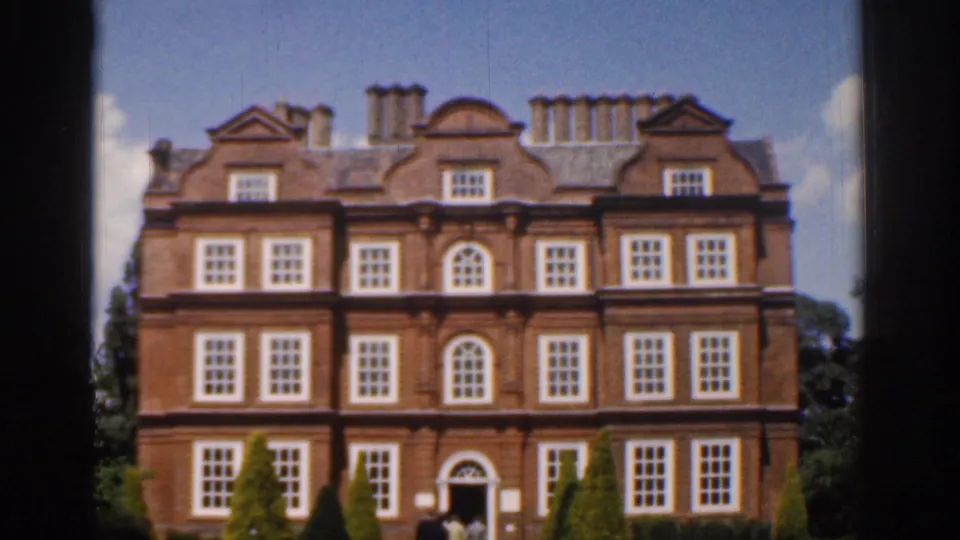 1961 Ireland 8mm frame showing a stately red brick mansion facade with white-trimmed windows, chimneys, and manicured shrubs.