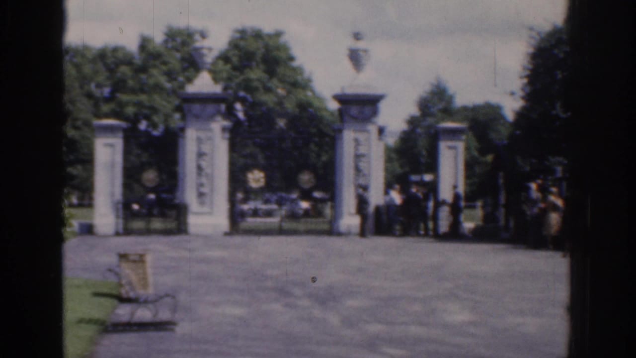 1961 Ireland 8mm frame showing an estate-style entrance with pale gate pillars, an open driveway, trees, and small figures near the gate.