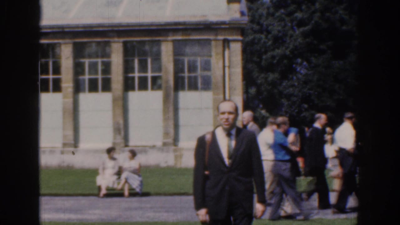 In 1961 Ireland home-movie footage, a suited man with a shoulder bag walks toward the camera in a public park.