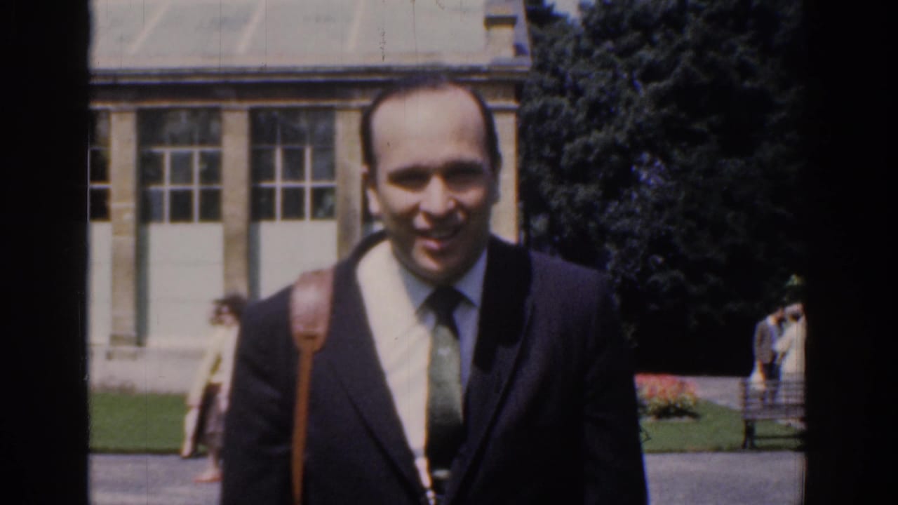 Close 1961 Ireland home-movie frame of the smiling suited man approaching the camera in a public park setting.