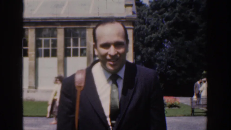 Close 1961 Ireland home-movie frame of the smiling suited man approaching the camera in a public park setting.
