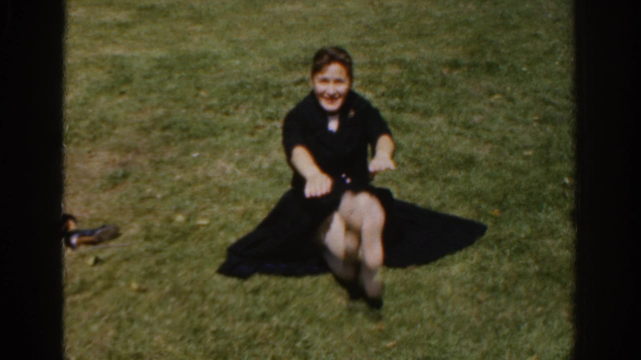 Woman in a dark dress sits on grass with legs raised during a sit-up.