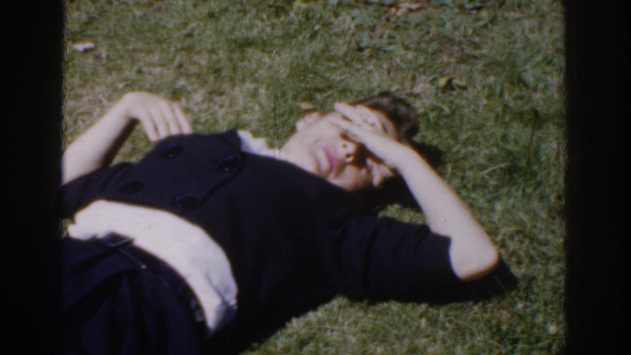 A closer 1961 Ireland home-movie frame shows the woman lying on grass with one hand shading her face.