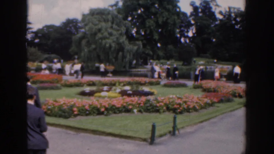 1961 Ireland home-movie view across formal flowerbeds and lawns with visitors walking along garden paths.