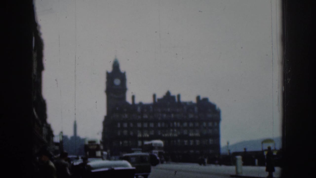 Hotel with clock tower across a street, with a bus, cars, pedestrians, and dark vertical foreground edges.
