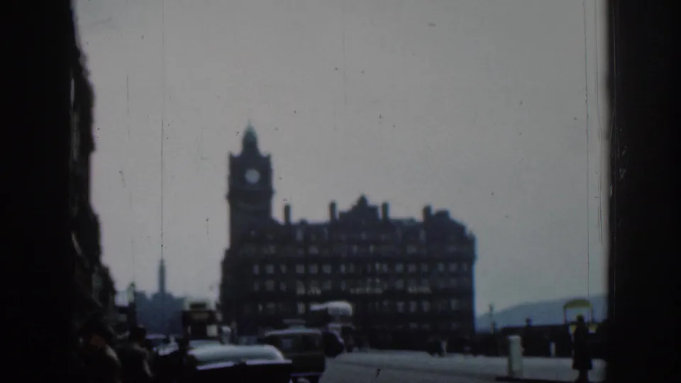 1961 London street view with a clock-tower hotel in the background, vintage traffic in front, and the scene framed by dark vertical edges.