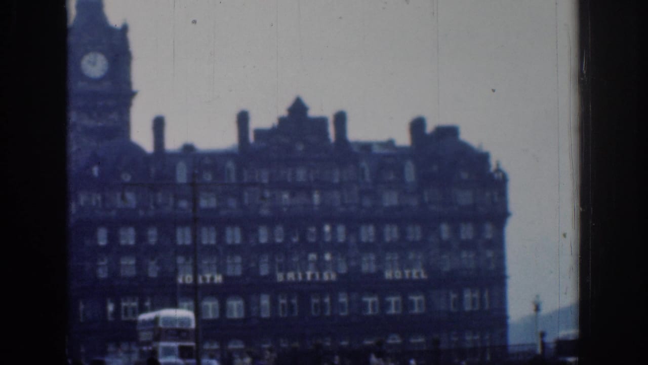 Closer 1961 London 8mm view of the clock-tower hotel facade, with lettering appearing to read North British Hotel and traffic at street level.