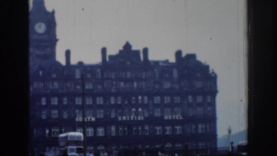 Closer 1961 London 8mm view of the clock-tower hotel facade, with lettering appearing to read North British Hotel and traffic at street level.