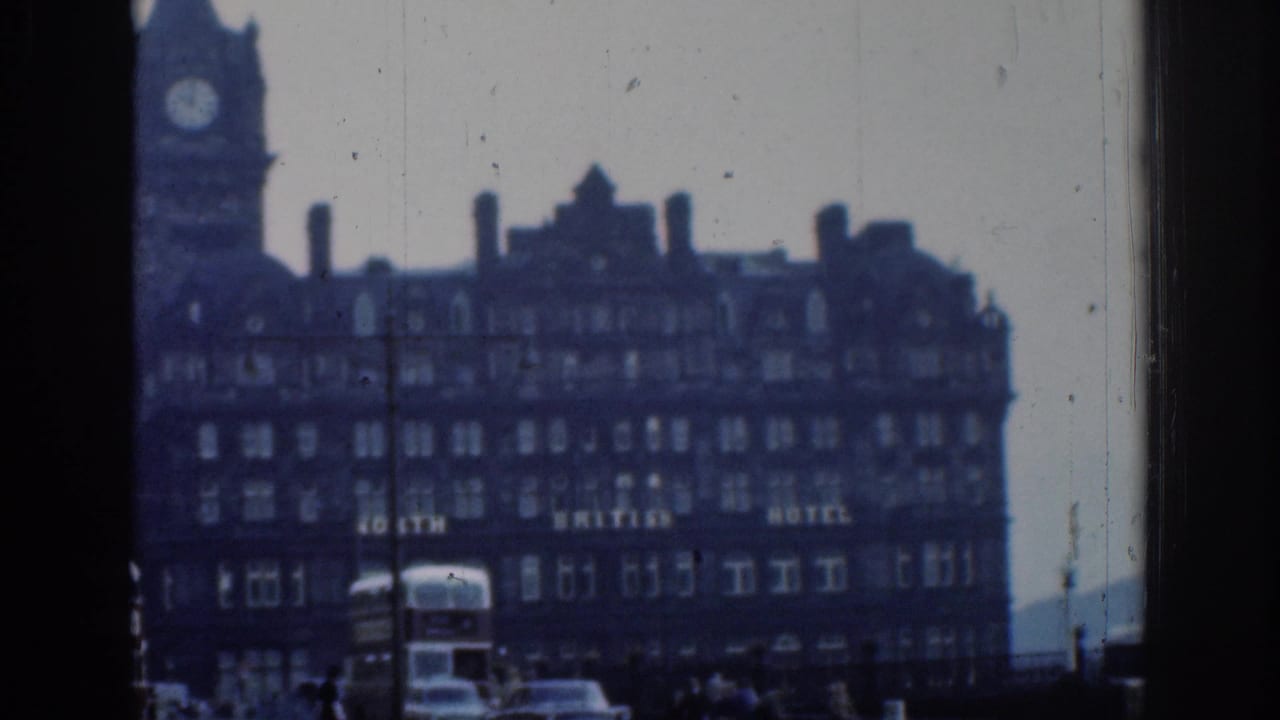 1961 London 8mm frame showing the hotel facade and clock tower with partial lettering, buses and cars below, and dark foreground framing.