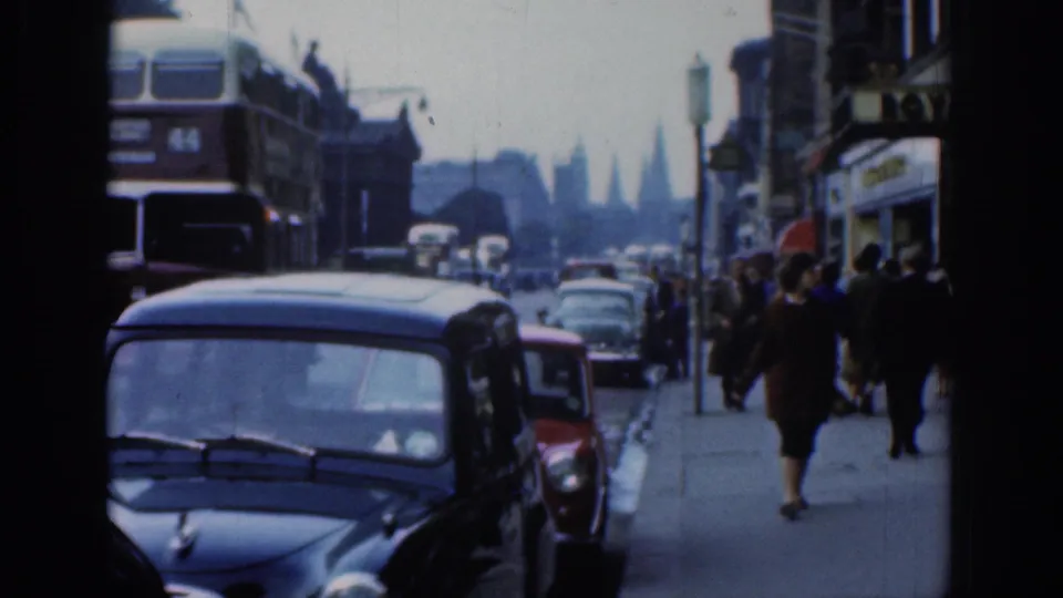 1961 London traffic view with a double-decker bus, compact cars, pedestrians on the pavement, shopfronts, and distant spires.