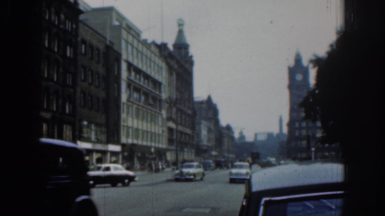 Wide London street with cars, buildings, trees, and a distant tower.