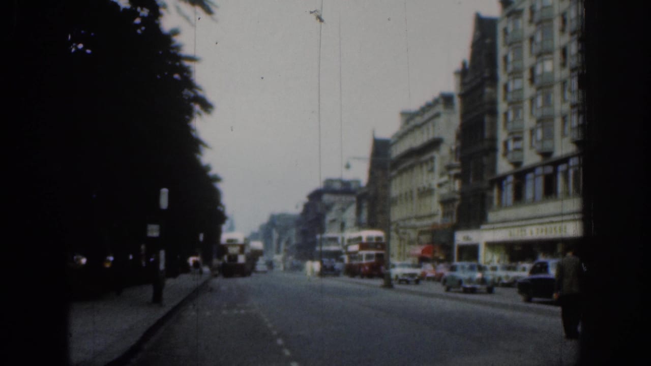 1961 London street view with double-decker buses, period cars, pedestrians, and tall buildings along a tree-lined avenue.