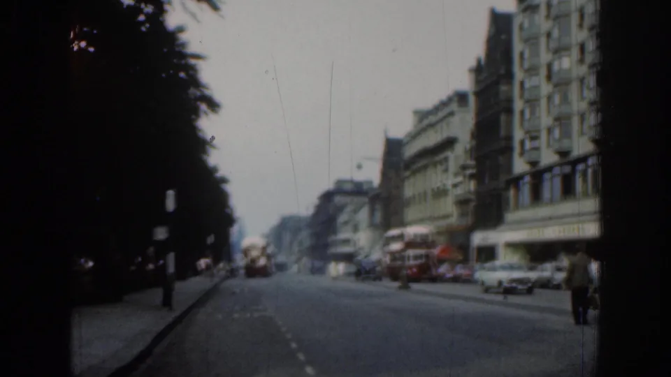 London avenue scene with red buses, cars, pedestrians, storefront buildings, and dark trees framing the road.