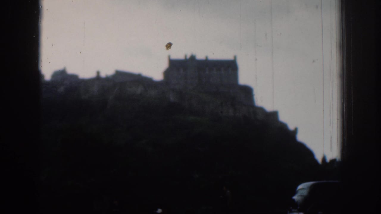 Distant castle-like structure on a hill, filmed in soft 8mm exposure with dark foreground trees and a partial vehicle below.
