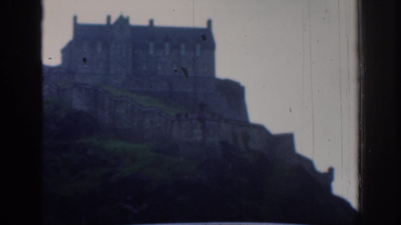Soft, scratched 8mm frame of the metadata-identified Edinburgh Castle on its rocky rise, viewed from a roadside or windowed position.