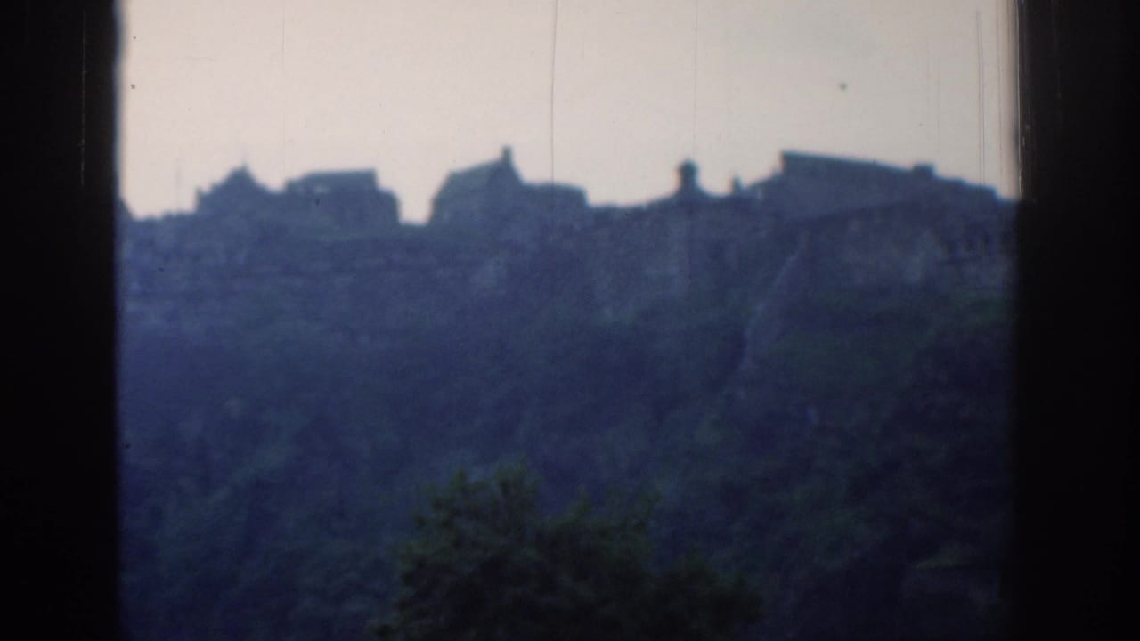 1961 London home-movie frame with silhouetted buildings on a forested ridge under a pale sky.