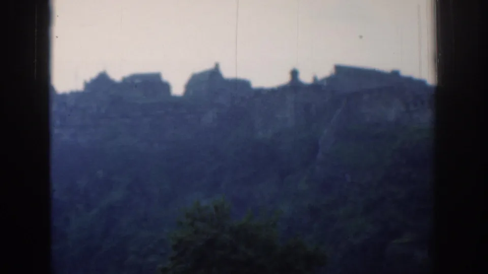 1961 London home-movie frame with silhouetted buildings on a forested ridge under a pale sky.