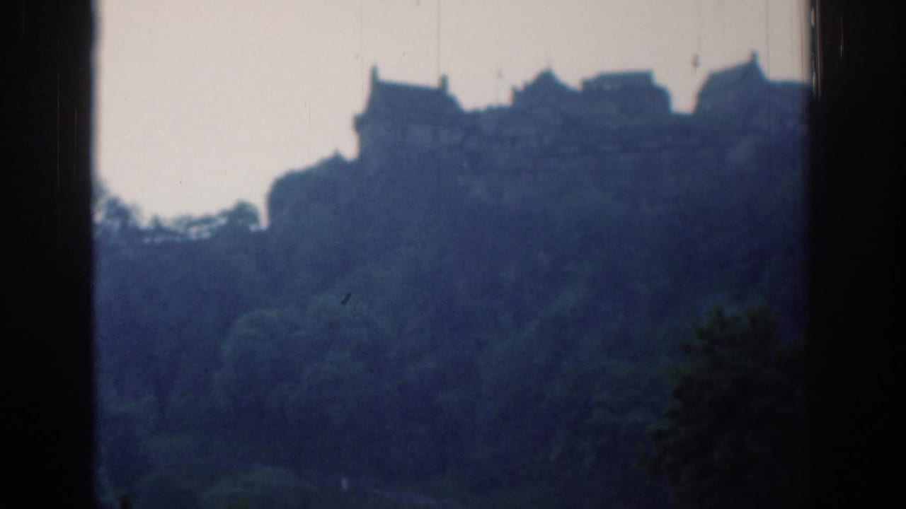 1961 London 8mm frame showing a static distant view of buildings above dense trees and dark side borders.