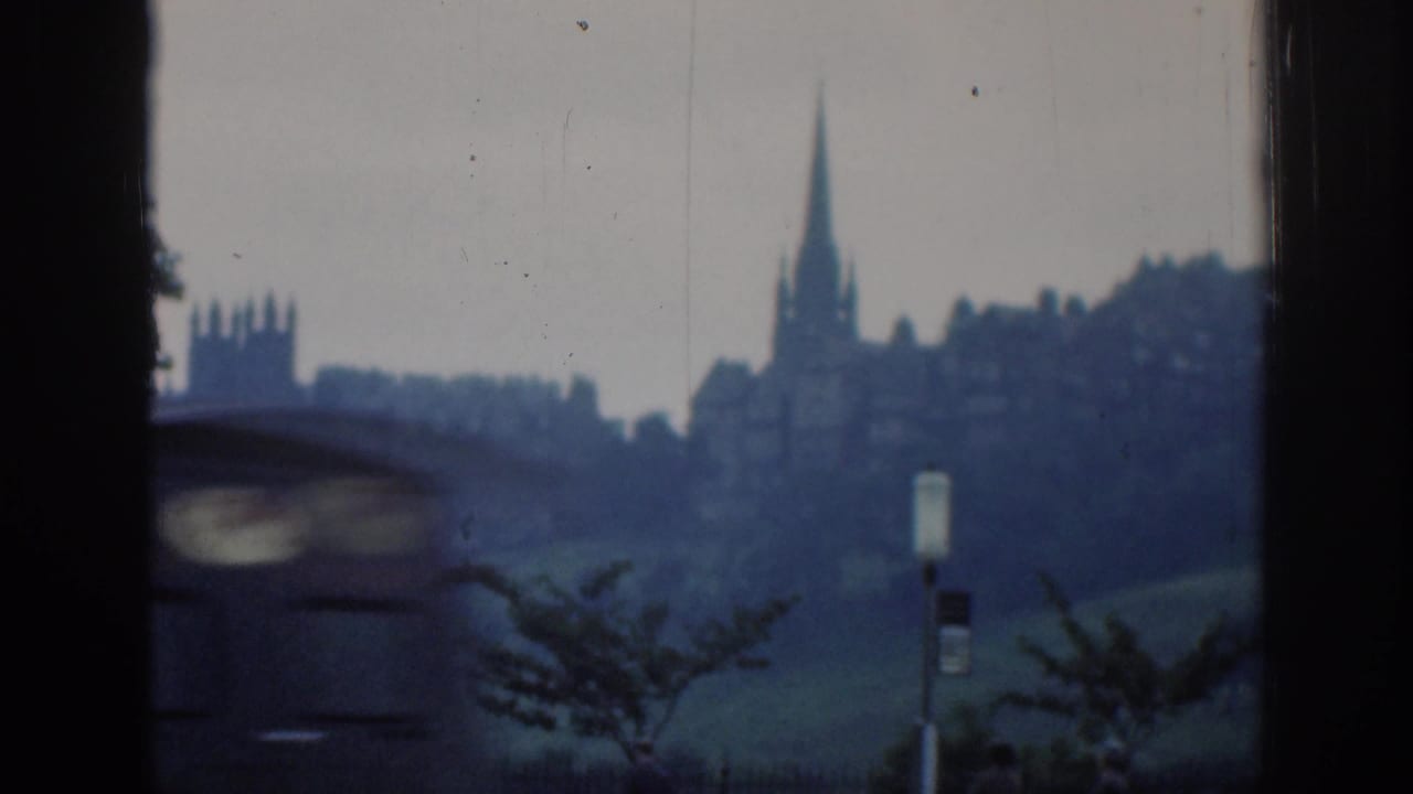 A blurred car passes the foreground as 1961 London architecture and a tall church spire remain visible across a green hillside.