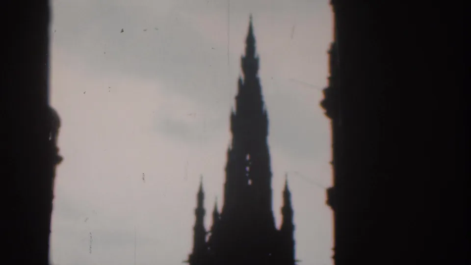1961 London 8mm frame showing a tall spire in dark silhouette against a pale sky, viewed through a shadowed opening.