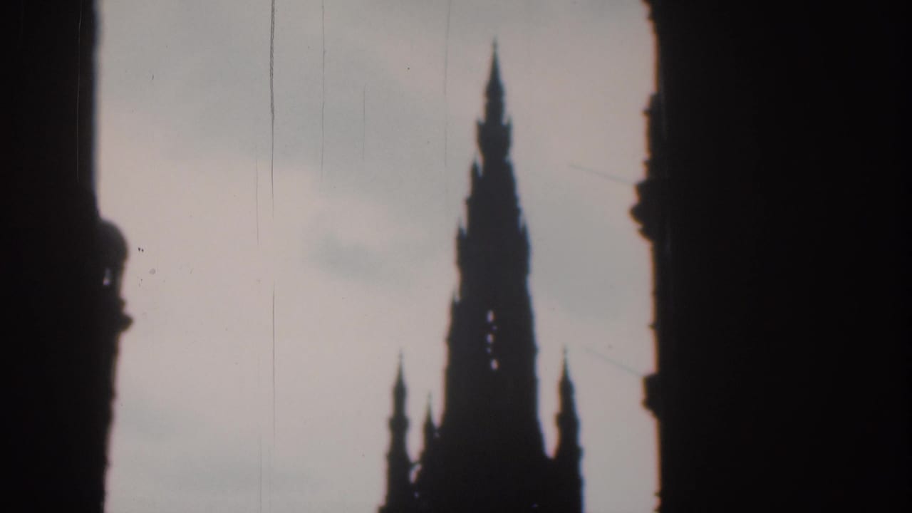 Dark foreground buildings frame a tall Gothic spire against a pale sky.