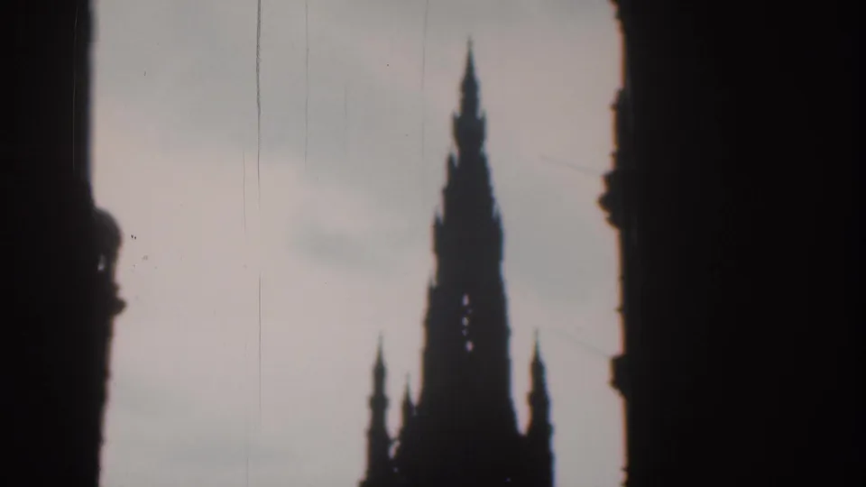 1961 8mm footage cataloged to London shows a Gothic monument spire silhouetted between dark urban structures.