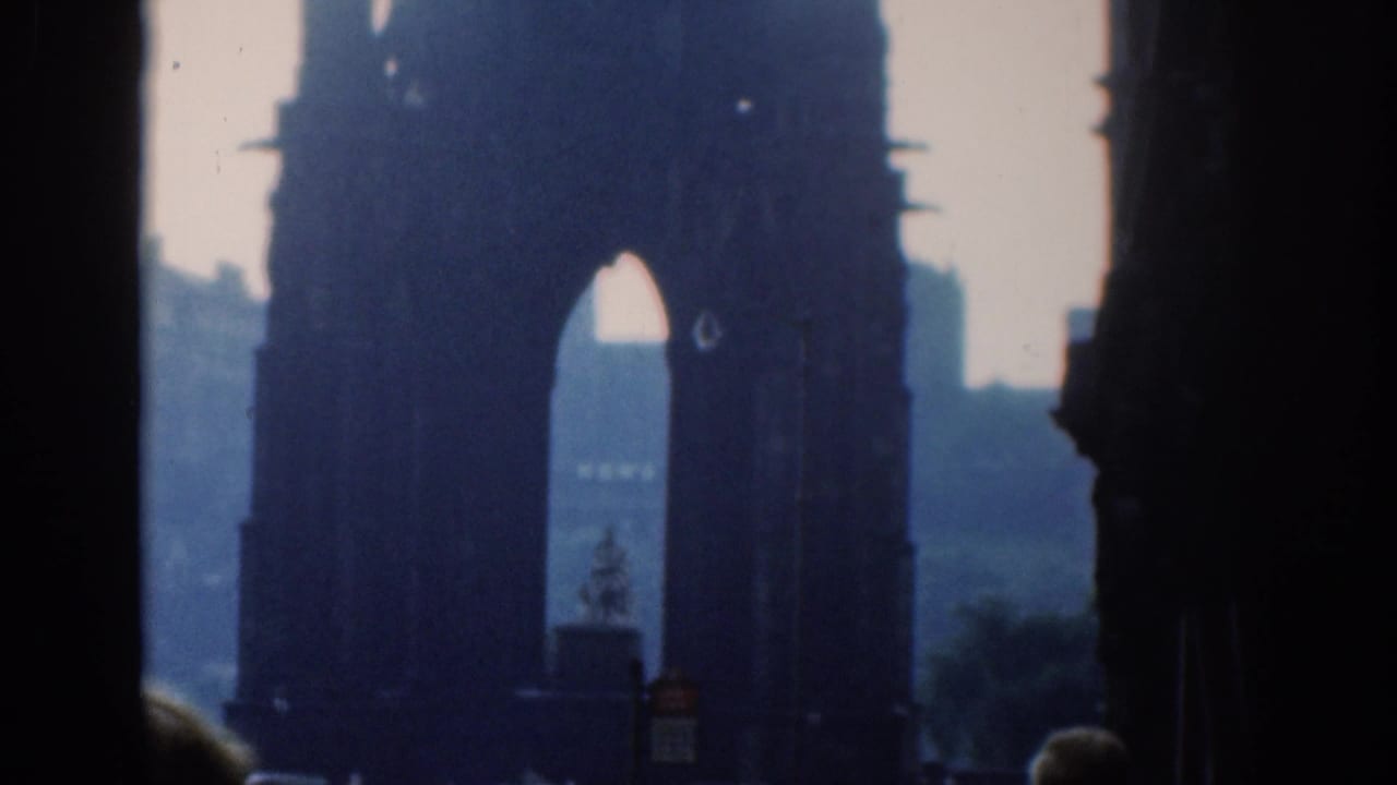 A closer, blue-toned 8mm frame shows the Gothic arch tower, distant buildings, and small street silhouettes below.