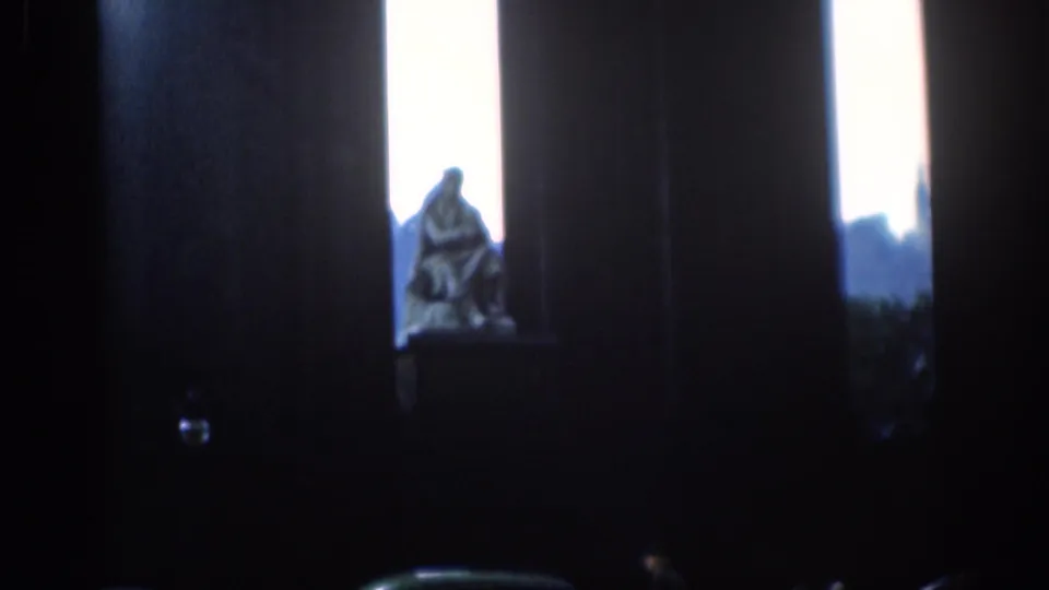 1961 London 8mm view of a seated statue framed by dark columns and bright sky beyond.