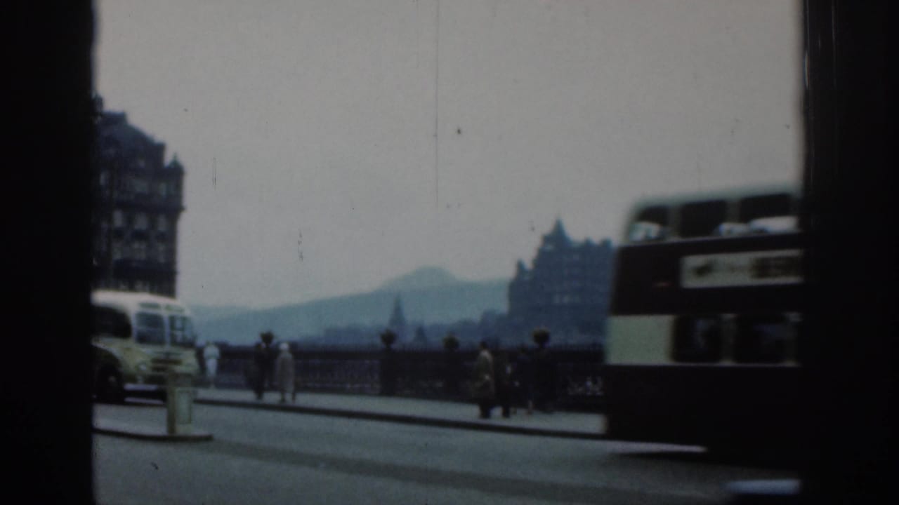 London street traffic passing a bridge with buses, cars, pedestrians and distant buildings.