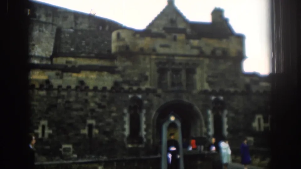 1961 London visitor footage frames a castle-like stone entrance with a guard standing post as tourists pass nearby.