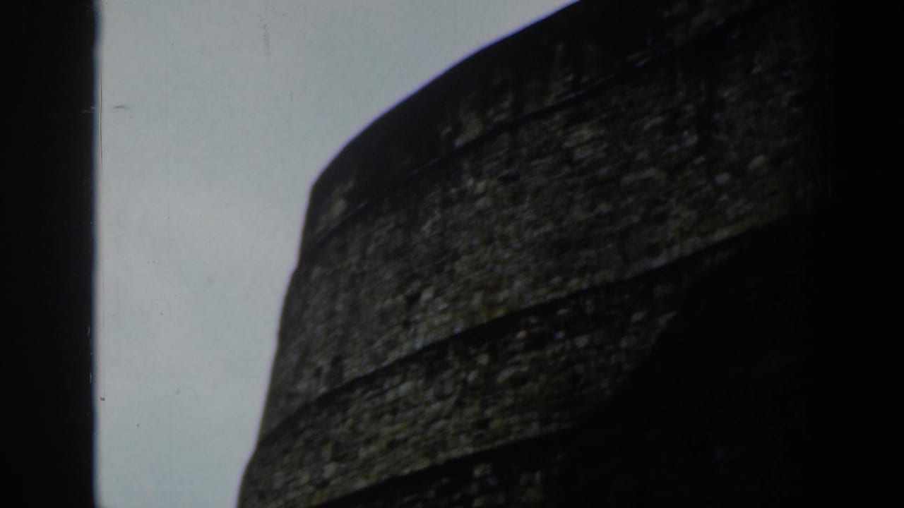 Close view of a dark, weathered stone wall against a pale sky.