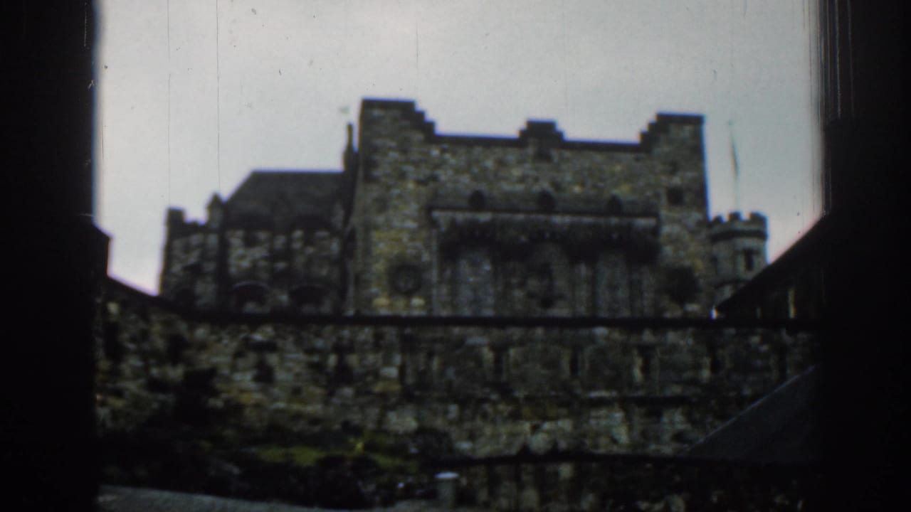 1961 London visitor-shot frame showing a wider view of a historic stone structure with battlements, towers, and dark foreground framing.