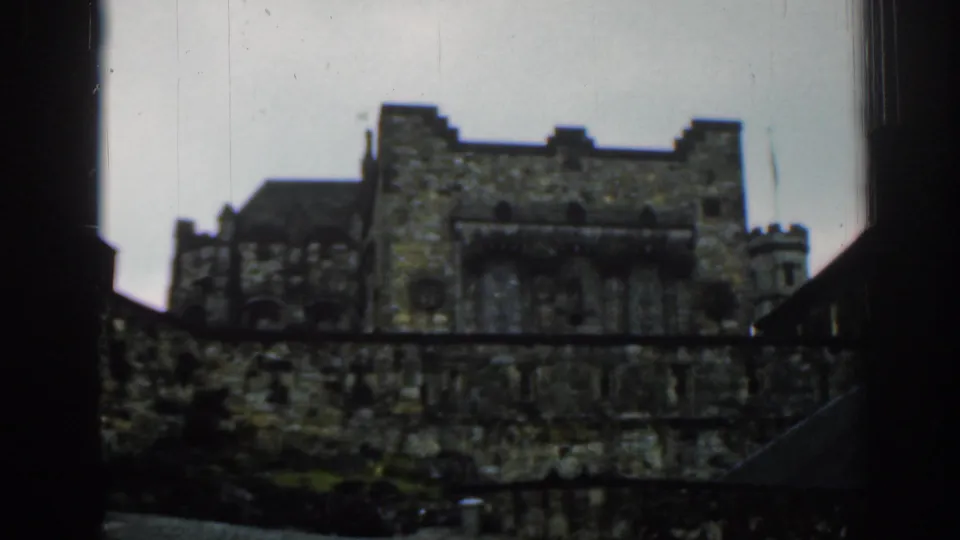 1961 London visitor-shot frame showing a wider view of a historic stone structure with battlements, towers, and dark foreground framing.