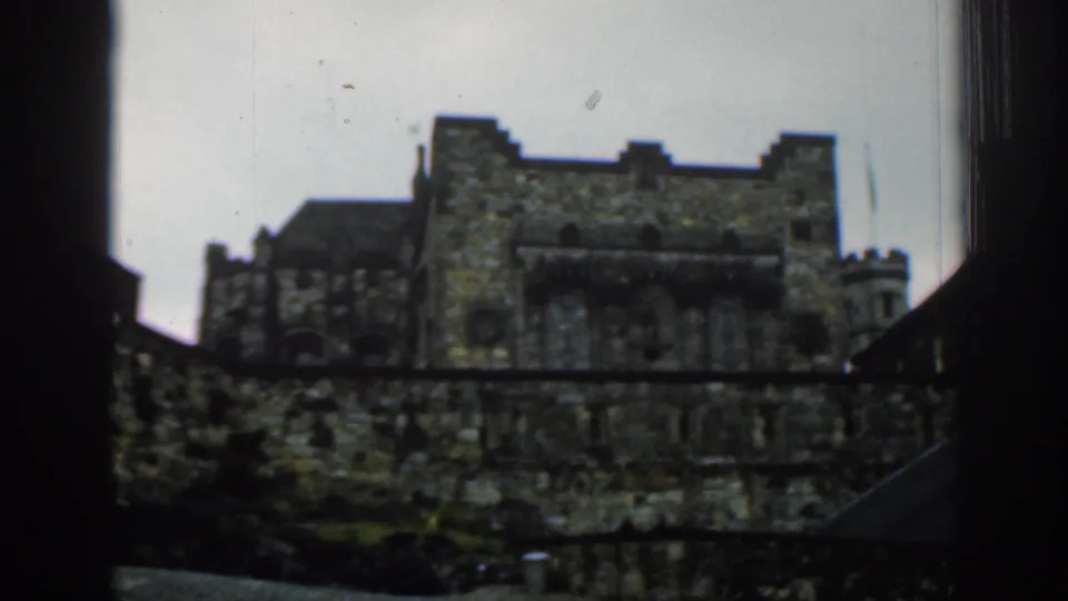 1961 London home-movie frame showing a weathered stone monastery-like building seen through dark film borders.