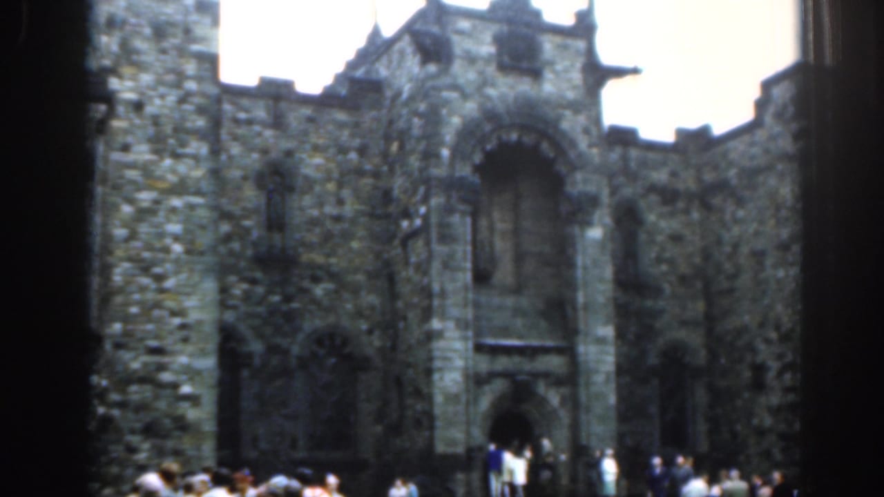 Stone castle facade with arched entrance and tourists gathered below.