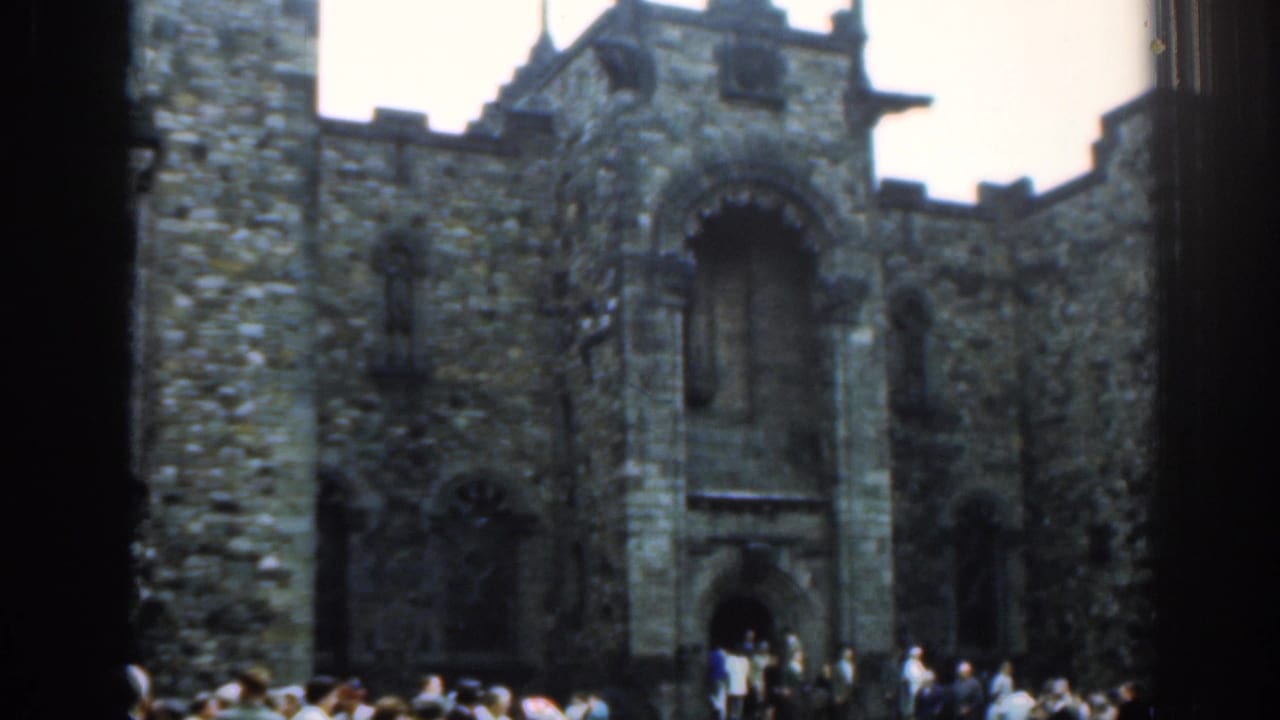 Crenellated stone building with tourists standing near an arched doorway.