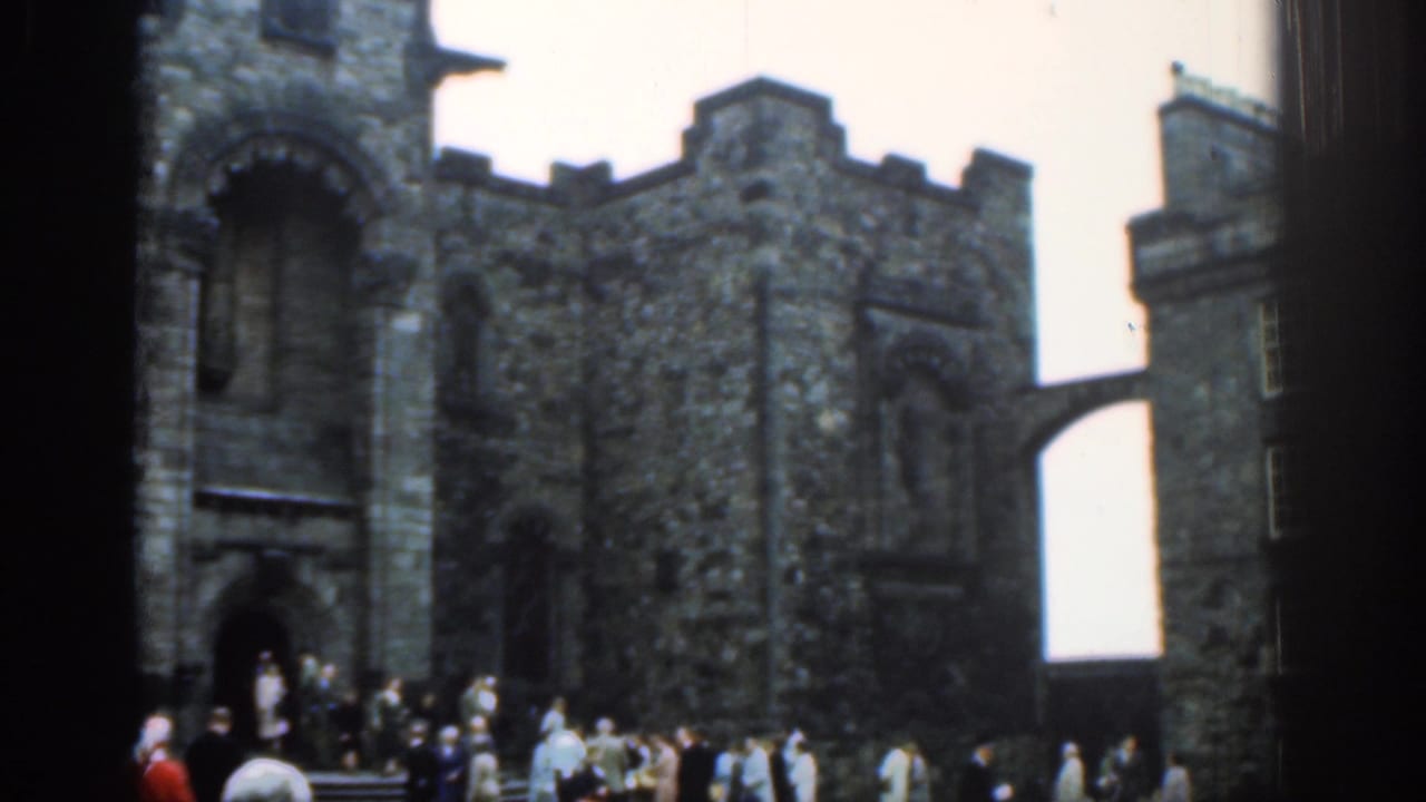 1961 London home-movie view of a stone castle wall, tower, elevated passage, and tourists moving across the foreground.