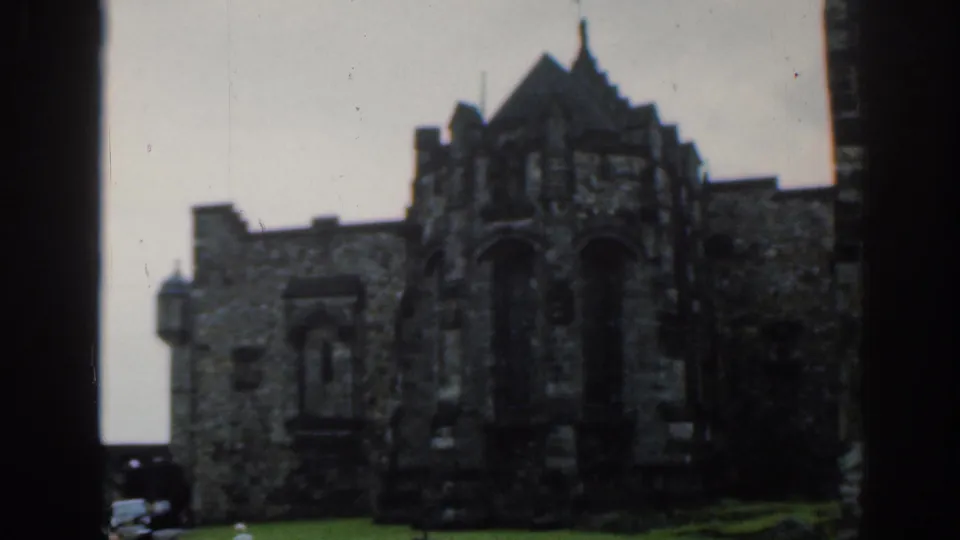 Wider 1961 London home-movie view of the church exterior, showing a stone facade, dark arched entrance, and grass foreground.